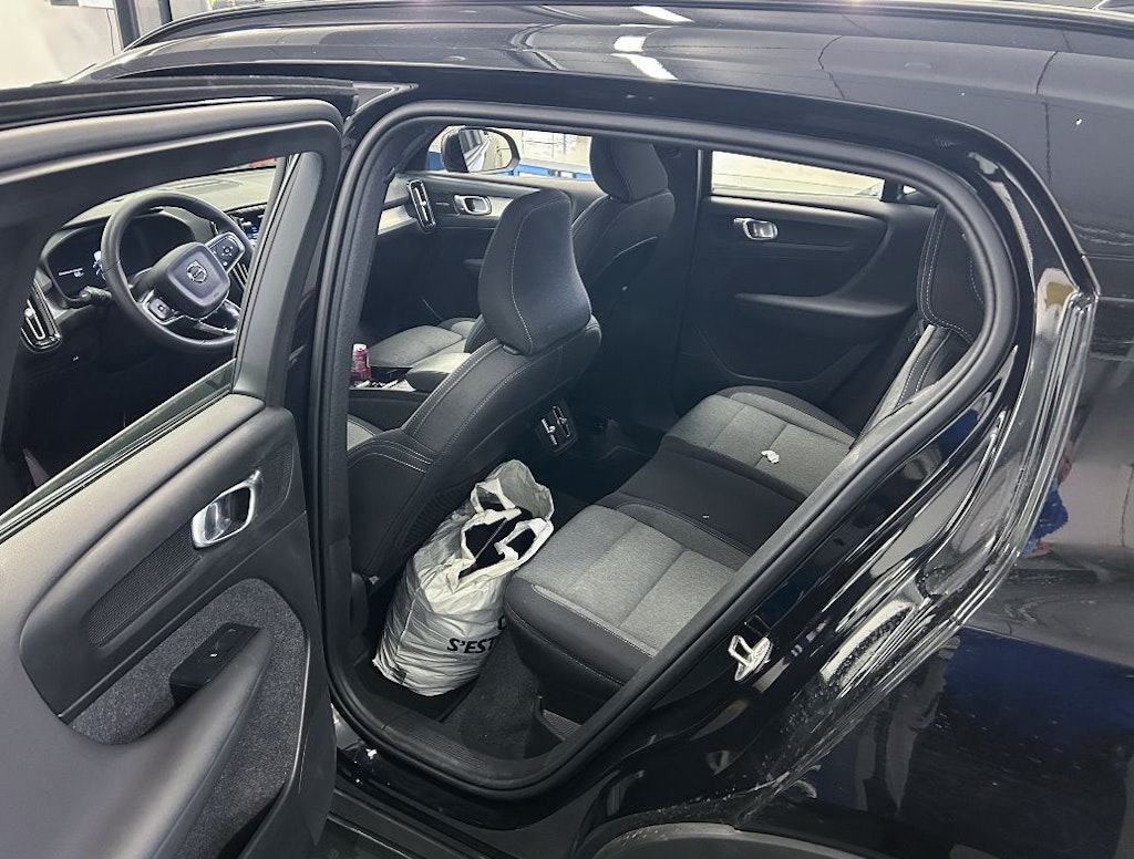 L'intérieur d'une voiture avec la porte ouverte montre un siège passager et un siège arrière. Un sac blanc est posé sur le siège arrière.