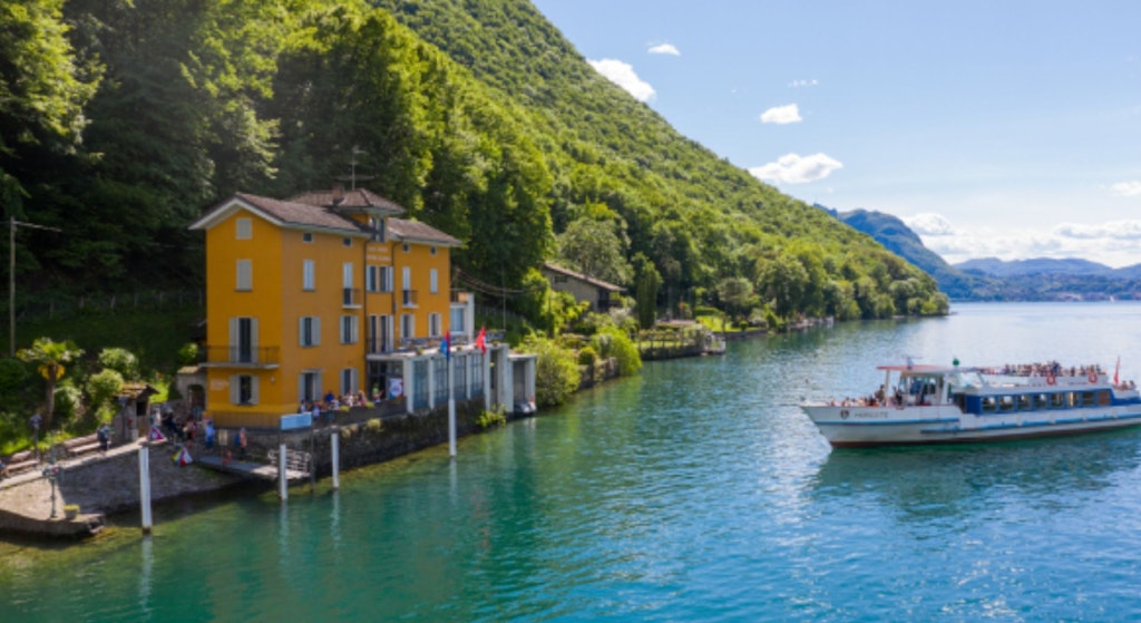 Un bateau passe devant un bâtiment jaune au bord d'un lac.