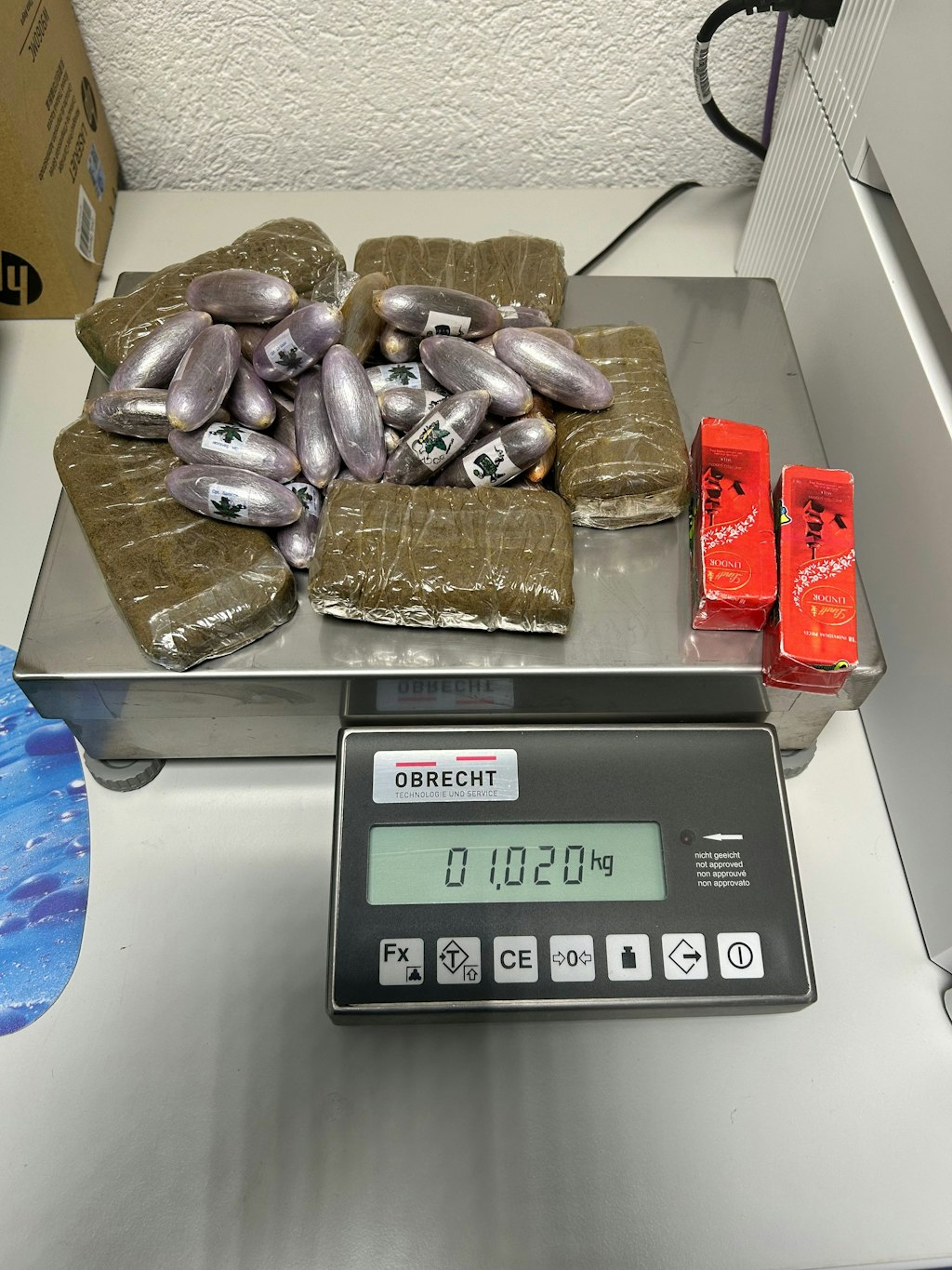 Plusieurs paquets de haschisch et capsules sont posés sur une balance. La balance indique un poids de 1,020 kg.