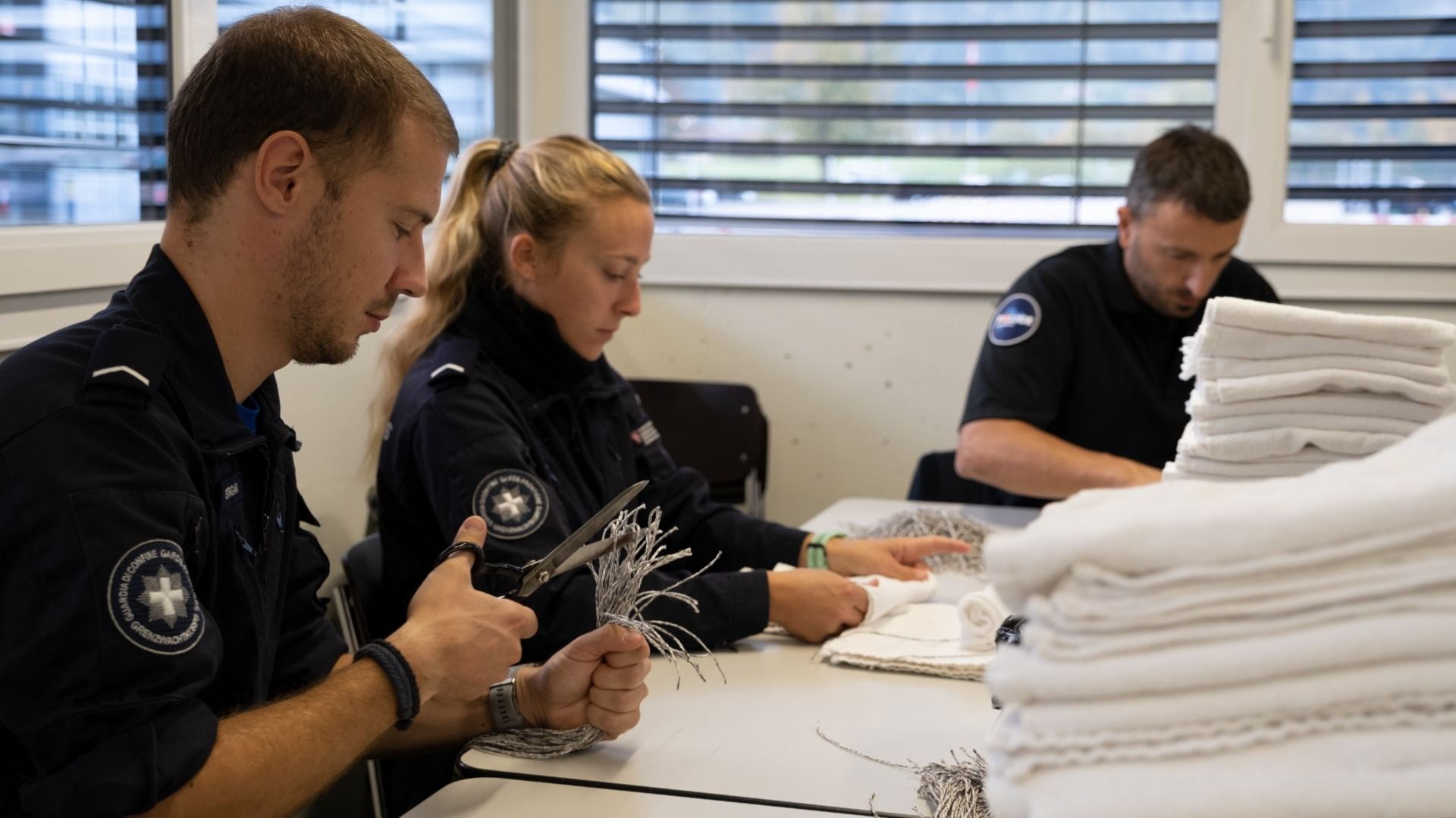 Trois personnes en uniforme travaillent à une table avec des serviettes éponge et des cordes. Ils lient des "Muffs" pour la journée de formation. 