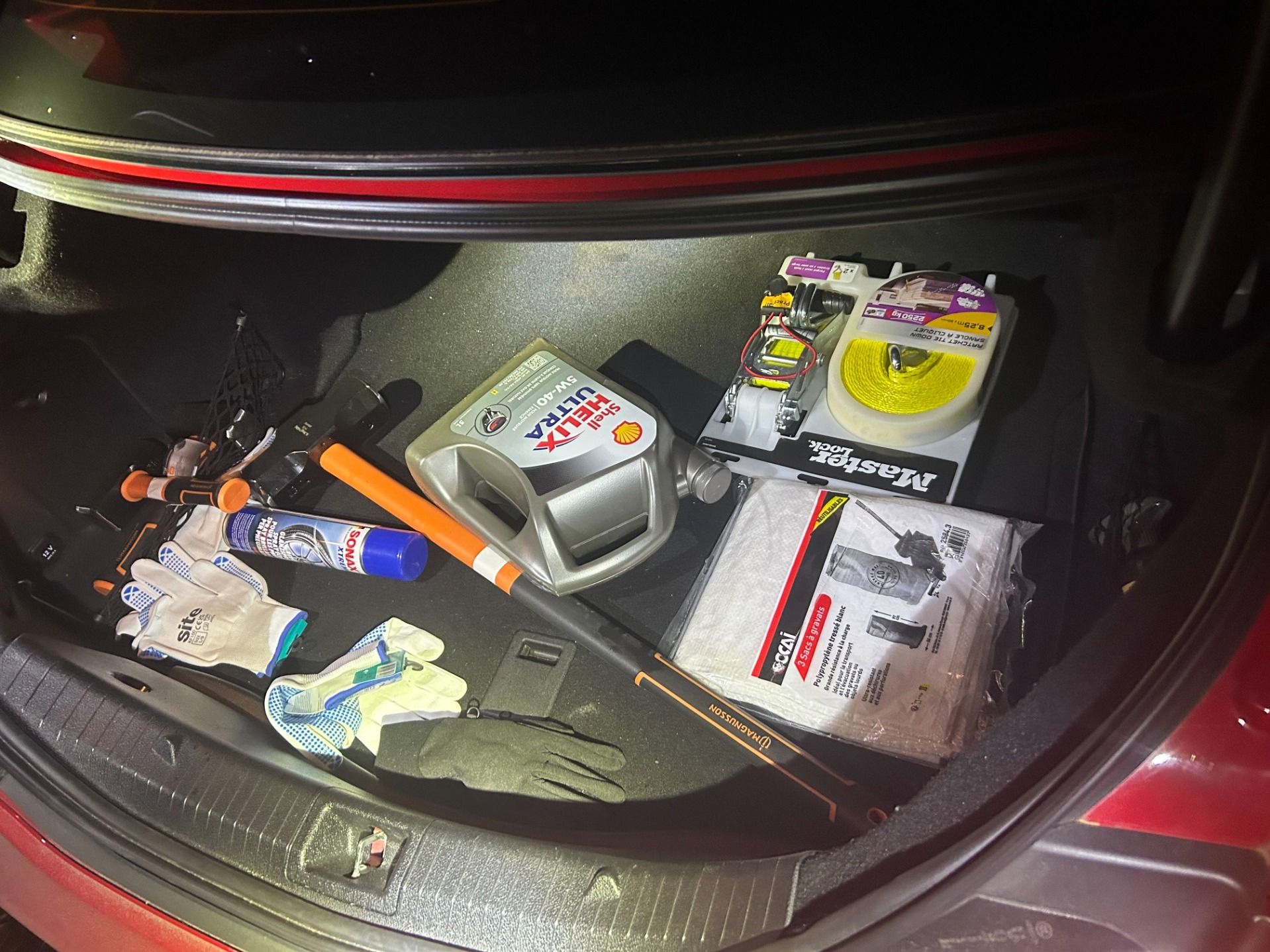 Divers outils, gants, bidon d'huile moteur, sangle et autres objets sont visibles dans le coffre d'une voiture. Ces objets pourraient servir à commettre des cambriolages.