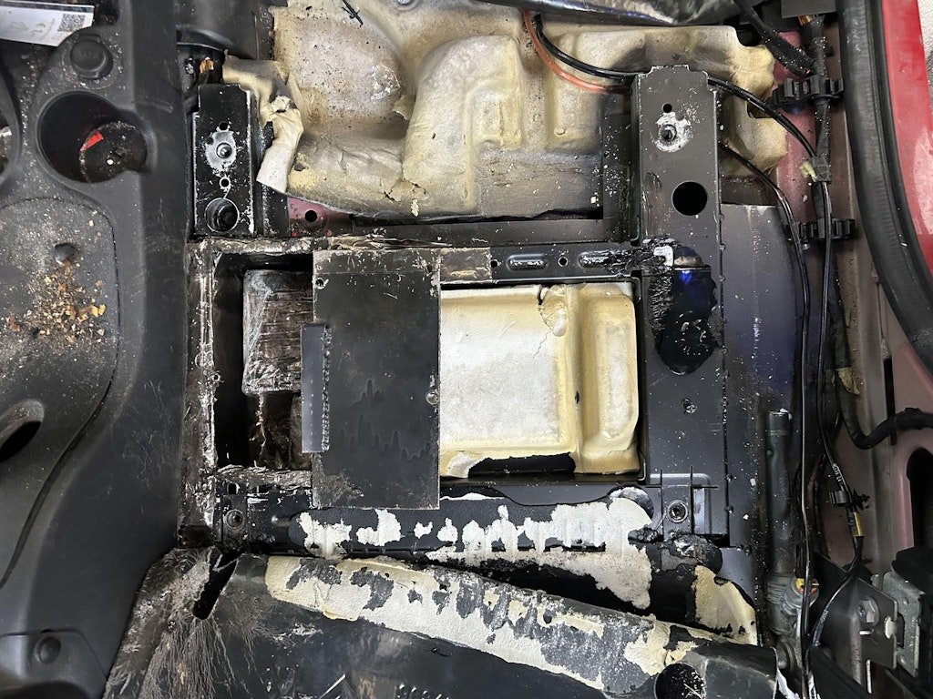 Un compartiment caché dans un véhicule avec une plaque métallique au-dessus. L'environnement montre des signes de manipulation et d'usure.