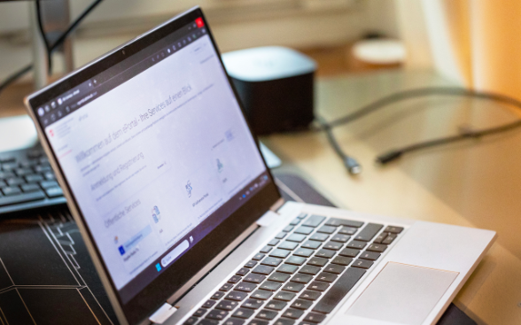 Un ordinateur portable ouvert affiche la page d'accueil de la plateforme fiscale « Taxas » avec différents services numériques. L'écran est légèrement flou, mais la structure de la plateforme est visible.