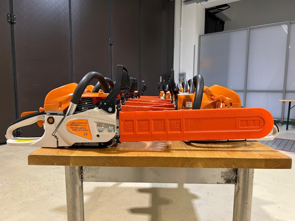 Diverse motoseghe arancioni sono allineate su un tavolo di legno. Le motoseghe sono nuove e protette da coperture.