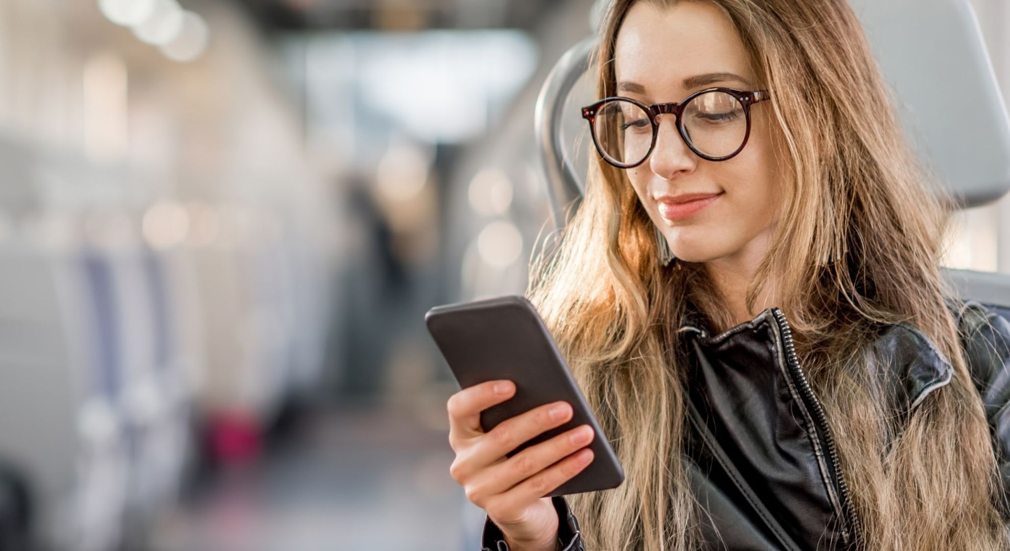 Giovane donna seduta sul treno che guarda il suo smartphone