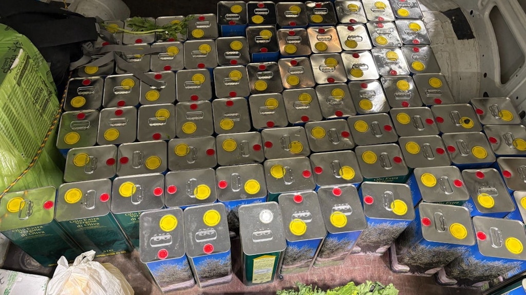 Diversi contenitori di olio d'oliva sono impilati in un veicolo. I contenitori hanno tappi gialli e rossi.