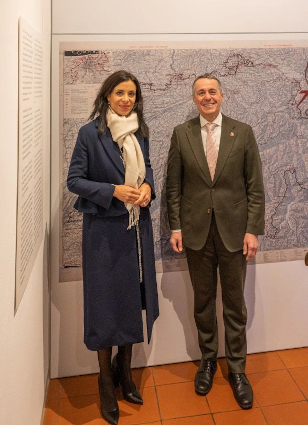 Due persone elegantemente vestite stanno in piedi una accanto all'altra davanti a una grande mappa storica in una sala espositiva. Guardano l'obiettivo e posano per una foto ufficiale.