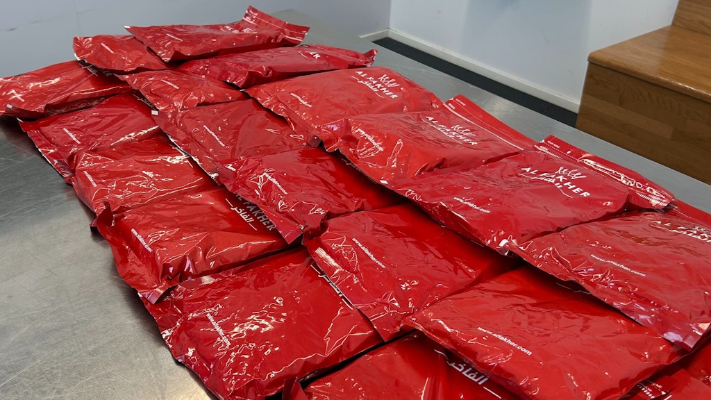 Diverse confezioni rosse di tabacco Al Fakher sono impilate su un tavolo. Le confezioni sono lucide e mostrano il nome del marchio.  