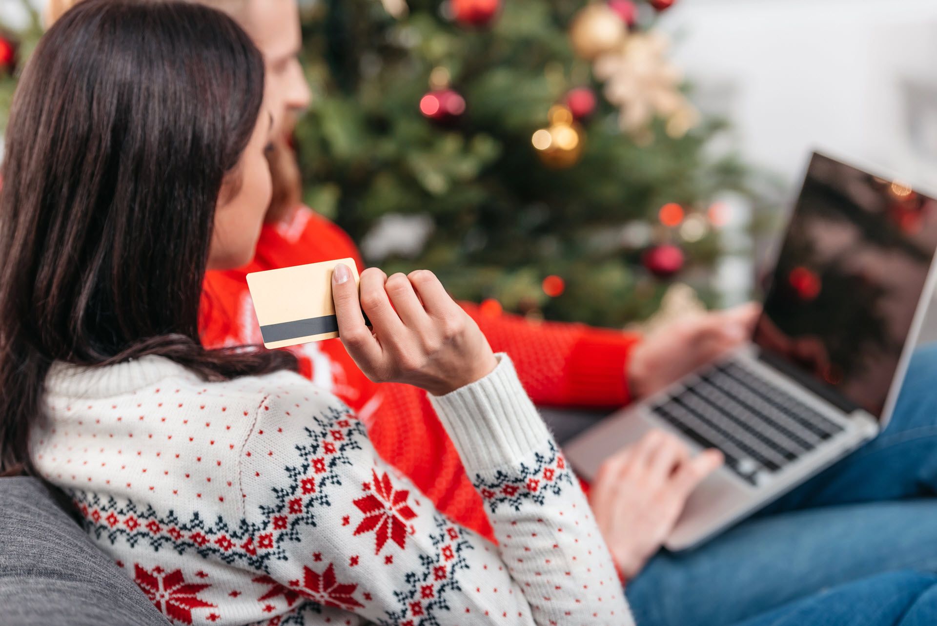 Una persona tiene una carta di credito e utilizza un laptop davanti a un albero di Natale