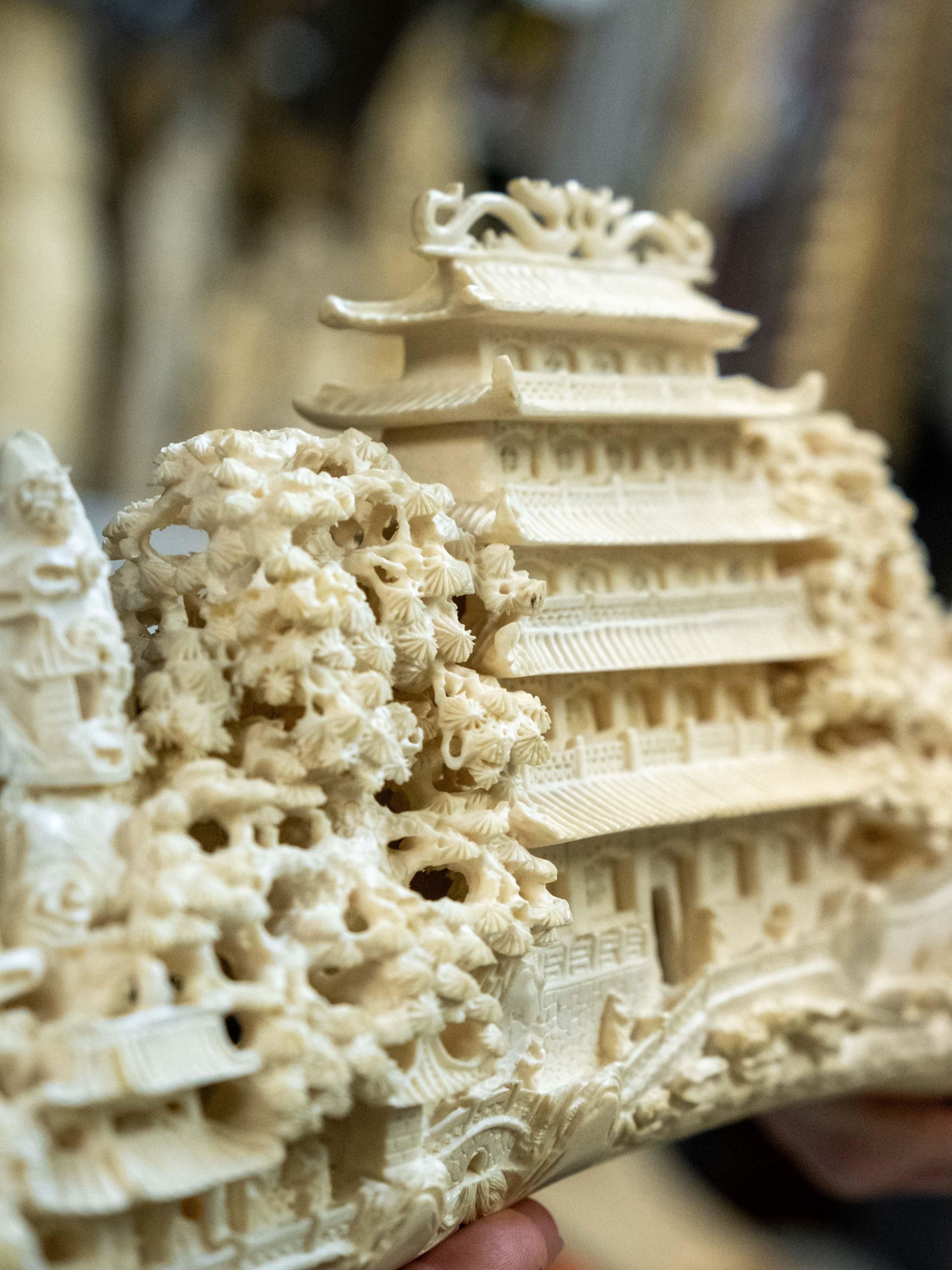 Un tempio intagliato in avorio con ornamenti dettagliati e tetti ricurvi. La scultura evidenzia i dettagli raffinati dell'architettura e del paesaggio.