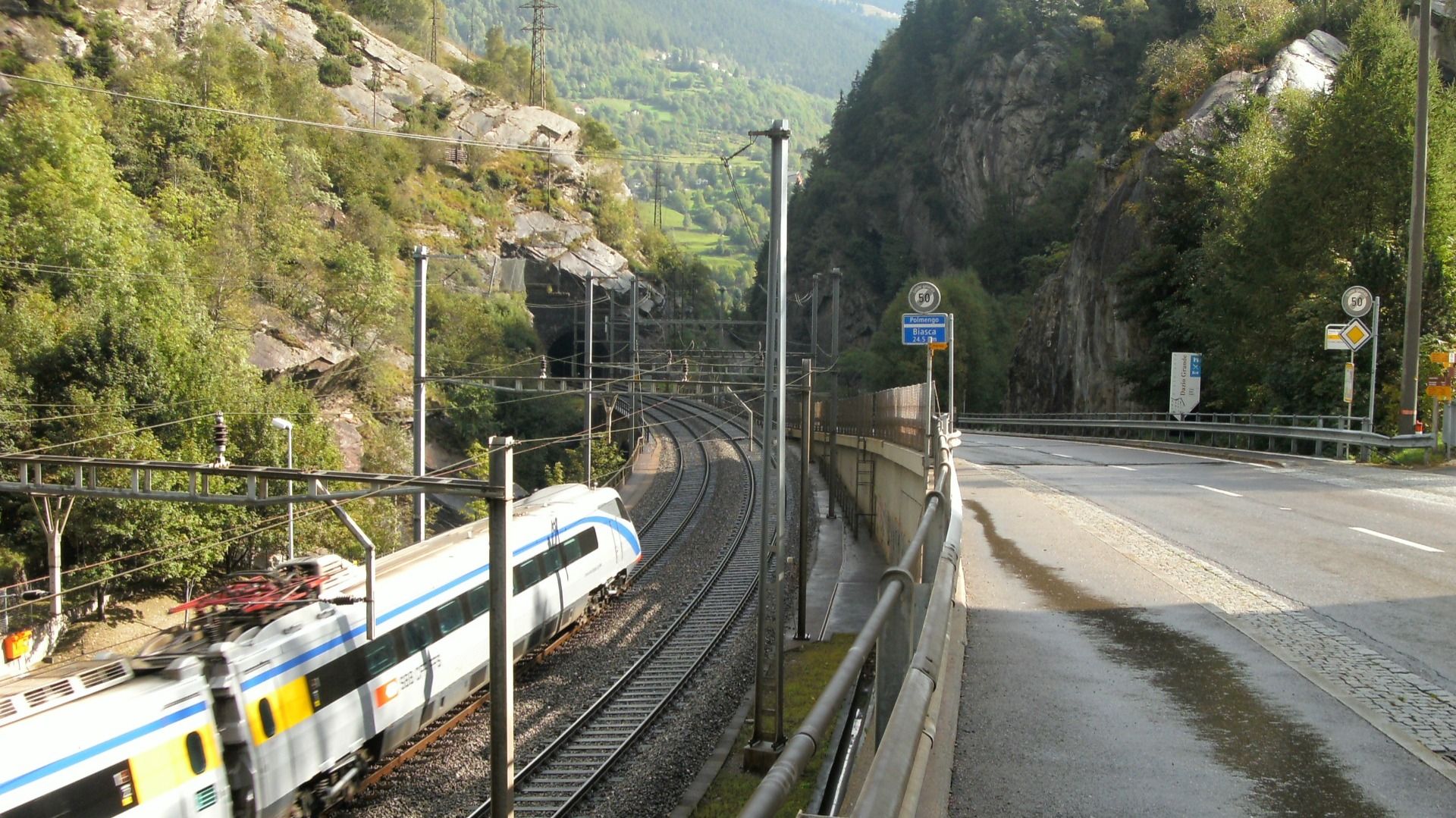 Un treno attraversa un tunnel in un paesaggio montuoso. L'ambiente è verde e roccioso.  