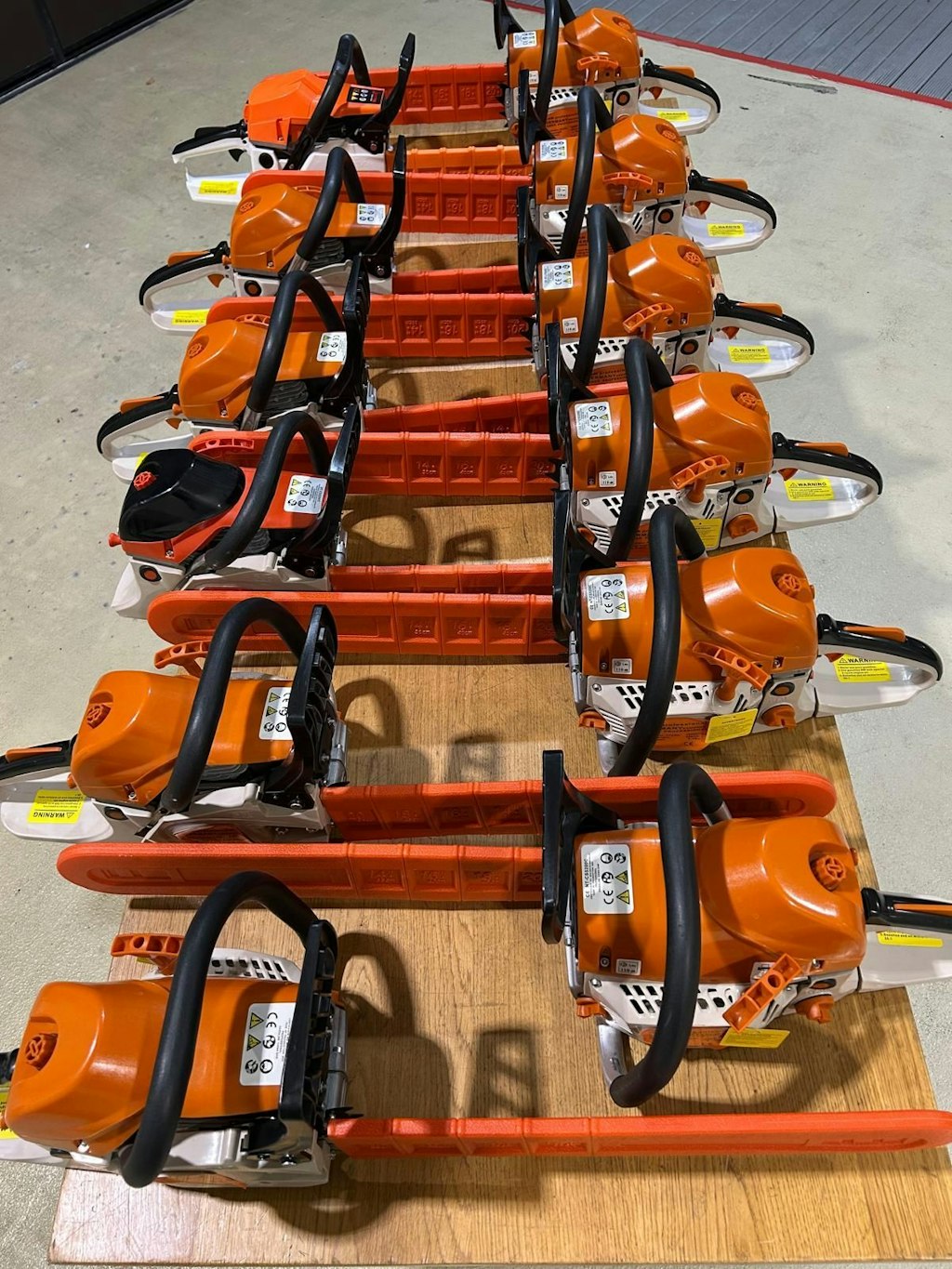 Diverse motoseghe arancioni sono disposte ordinatamente su un tavolo. Ogni catena e coperta da una protezione di sicurezza.