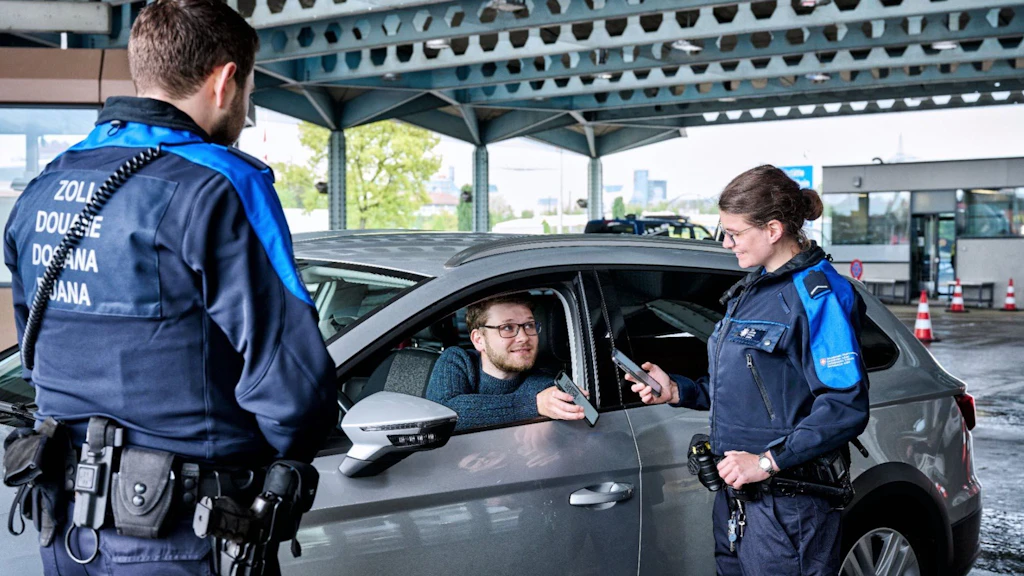 Due doganieri controllano un automobilista a un valico di frontiera. Il conducente mostra i suoi documenti.  