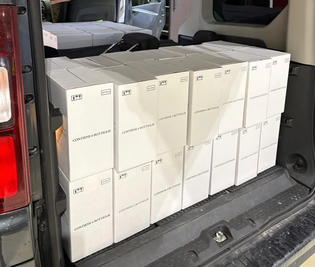 Numerose scatole contenenti ciascuna sei bottiglie di vino sono impilate in un'auto. Le scatole sono sistemate ordinatamente nel bagagliaio e sul sedile posteriore.